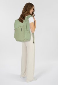 Zaino Thule verde con un design strutturato, tasca frontale con zip e spallacci imbottiti. Il materiale sembra resistente con una texture liscia.
