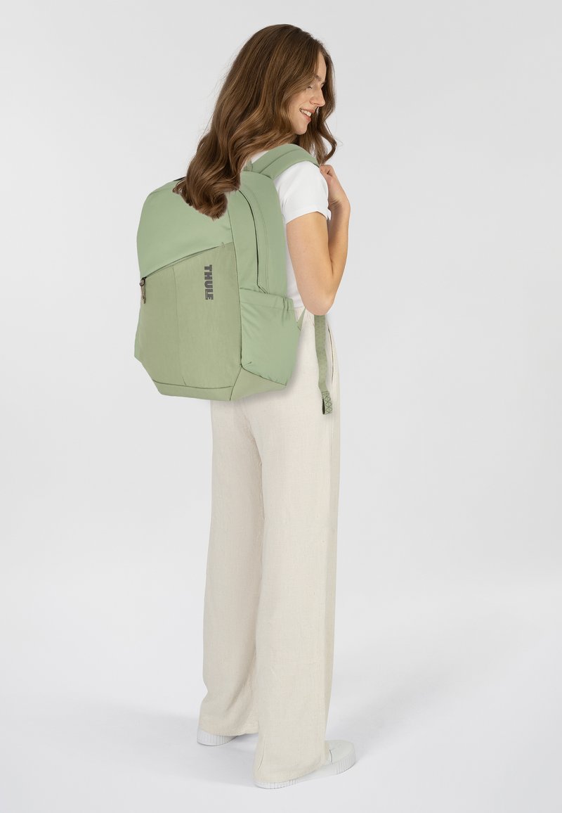 Zaino Thule verde con un design strutturato, tasca frontale con zip e spallacci imbottiti. Il materiale sembra resistente con una texture liscia.