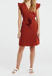 Röd klänning med v-ringning, korta volangärmar och ett knytbälte i midjan, med ett subtilt mönster av svarta prickar.