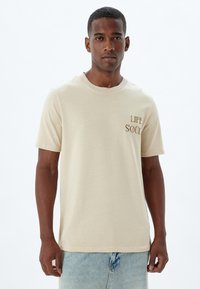 Beige kortemouwen t-shirt van katoen met een ronde hals, voorzien van bruine geborduurde tekst "LIFE" en "SOUL" op de linkerborst.