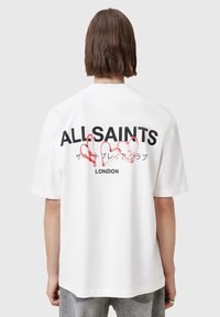 White oversized t-shirt with short sleeves, featuring bold black text "ALLSAINTS" and red heart graphics on the back. Casual cotton fabric.