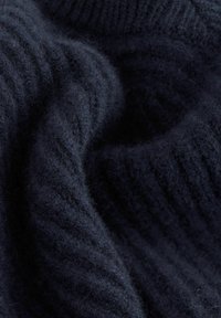 Zbliżenie miękkiej, ciemnoniebieskiej wełny, z widocznymi włóknami i żeberkową teksturą, tworzącą delikatne fałdy.