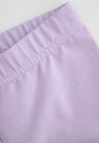 Jasnofioletowa tkanina o gładkiej teksturze, z marszczonym pasem i szytymi szwami. Zbliżenie na detal materiału.