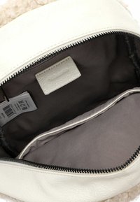 Intérieur d'un sac à main en simili cuir blanc avec doublure grise, comportant une poche en tissu et une étiquette avec le nom de la marque. Fermeture éclair sur le dessus.