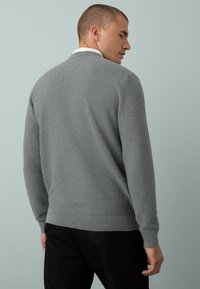 Suéter gris de punto con un acabado texturizado, mangas largas y puños acanalados. La parte de atrás presenta un diseño de cuello sutil y un dobladillo ajustado.