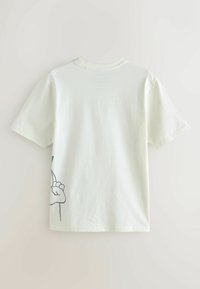 Tricou din bumbac verde deschis, cu mâneci scurte, având un design grafic cu o mână și o frunză pe lateral, textură netedă și croială lejeră.