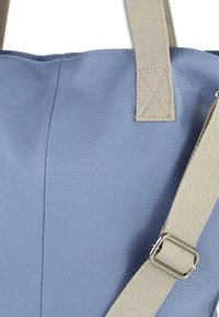 Blauwe leren boodschappentas met een gestructureerd oppervlak, beige canvasbanden en zilverkleurige metalen details. Heeft een verticale naad op het lichaam.