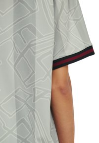 Ljust grå kortärmad skjorta med abstrakta geometriska mönster och en svart och mörkröd randig mudd synlig på en persons arm.