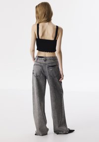 Top negro corto con dobladillo en forma de scallop, combinado con jeans de mezclilla gris, de pierna ancha y cintura alta, que presentan detalles desgastados y acentos de bolsillos.