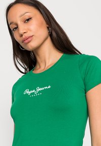 T-shirt verde ajustada, feita de algodão, com gola redonda, apresentando o logótipo branco "Pepe Jeans London" no peito. Manga curta, textura suave.