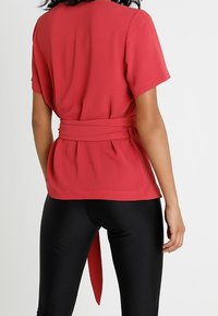 Haut rouge à manches courtes avec une taille ceinturée, caractérisé par une coupe ample et une texture lisse. Associé à des leggings noirs ajustés.