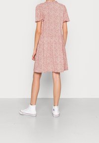 Robe courte rose à motifs floraux, manches courtes, taille froncée et jupe évasée, associée à des baskets blanches montantes.