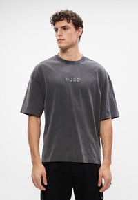 Graues Baumwoll-T-Shirt mit Rundhalsausschnitt, kurzen Ärmeln und einem geprägten "HUGO"-Logo auf der Brust. Weicher Stoff und entspannter Schnitt.
