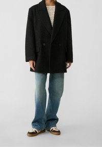 Abrigo negro de doble botonadura en lana texturizada, de corte oversized, con grandes solapas. Combinado con unos pantalones de mezclilla acampanados de color azul claro y zapatillas con estampado.