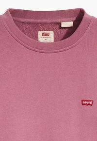 Rosa bomullströja med ribbad rund halsringning. Har en liten röd Levi's logotyp på vänster bröst. Storleksetikett i medelstorlek synlig.