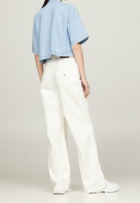 Light blue cropped denim shirt with short sleeves paired with high-waisted white wide-leg trousers and white sneakers.