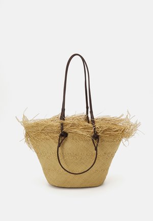Borsa tote in paglia intrecciata con manici in pelle marrone e un tocco di paglia frangiata attorno alla parte superiore, creando un design ampio e aperto.