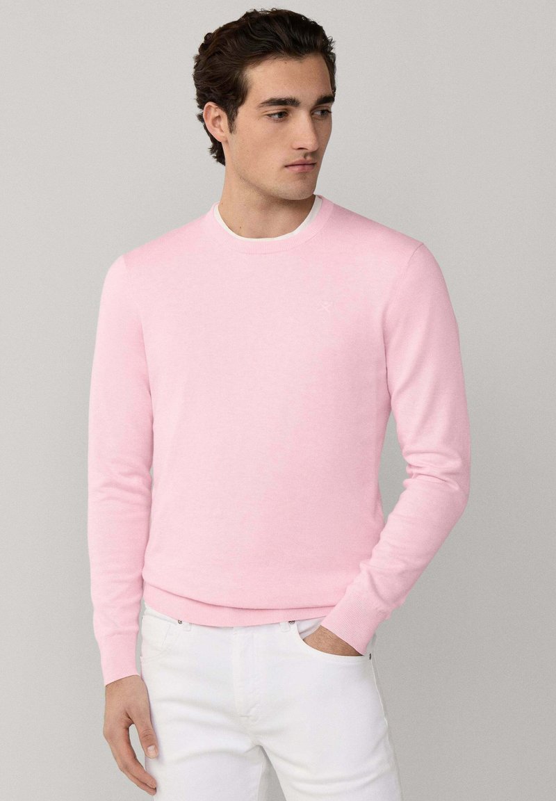 Maglione rosa chiaro in tessuto morbido a maglia, con scollo rotondo e polsini e orlo a coste, abbinato a pantaloni bianchi.