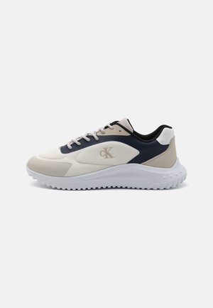 Zapatillas de hombre con parte superior de malla en blanco y azul marino, con acentos en crema. Suela blanca gruesa con banda de rodadura texturizada para mejor agarre.