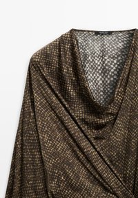 Braun und beige gemusterte Bluse mit Drapierung, V-Ausschnitt und locker fließendem Stoff auf einem weißen Hintergrund.