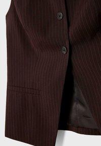 Burgundský vest s pruhovaným vzorem. Obsahuje dva černé knoflíky, nízký klopený límec a jedno náprsní kapsu. Hladká podšívka.