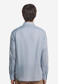 Ljusblå långärmad skjorta med tunna vita ränder, knäppte manschetter och klassisk krage. Mjukt tyg med avslappnad passform och bakveck.