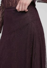 Jupe en dentelle bourgogne avec motifs floraux, présentant une taille lisse et une texture fluide. Gros plan montrant les détails complexes et le style du tissu.