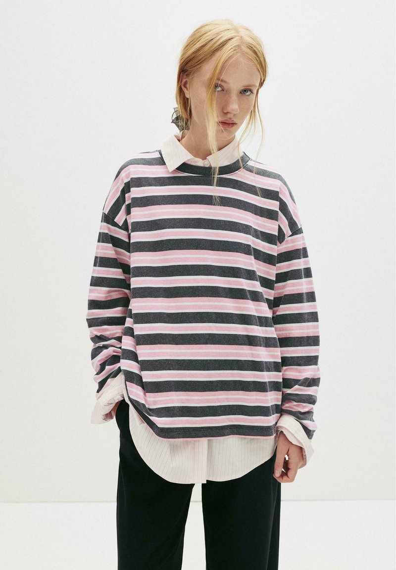 Stribet sweatshirt med rosa og marineblå vandrette striber, afslappet pasform, lavet af bomuldsmateriale, rund halsudskæring, lagdelt over en hvid skjorte med krave.
