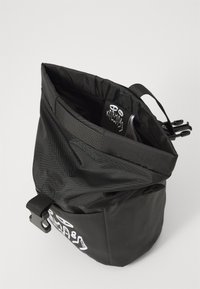Sac à cordon noir en nylon avec une surface texturée, étiquette de logo à l'intérieur et des sangles réglables à l'extérieur pour sécuriser les objets.