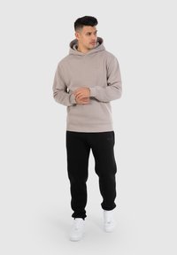 Lichtbeige hoodie met een voorzak en een capuchon met koord, gecombineerd met zwarte joggingbroek en witte sneakers. Eenvoudig ontwerp, zachte stof.