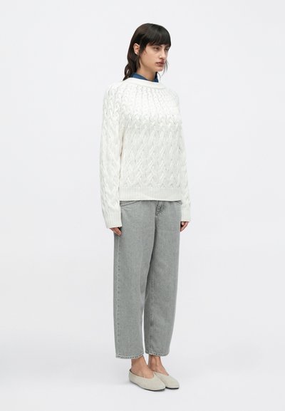 Λευκό πουλόβερ με πλέξη καλώ διο και στρογγυλή λαιμόκοψη, συνδυασμένο με άνετο γκρι τζιν και ανοιχτό γκρι μοκασίνια. Απλό, καθημερινό σύνολο.