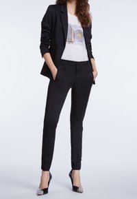 Blazer a scacchi neri con pantaloni su misura abbinati, abbinato a una t-shirt grafica bianca. Tacchi neri con dettagli argentati sulla punta.