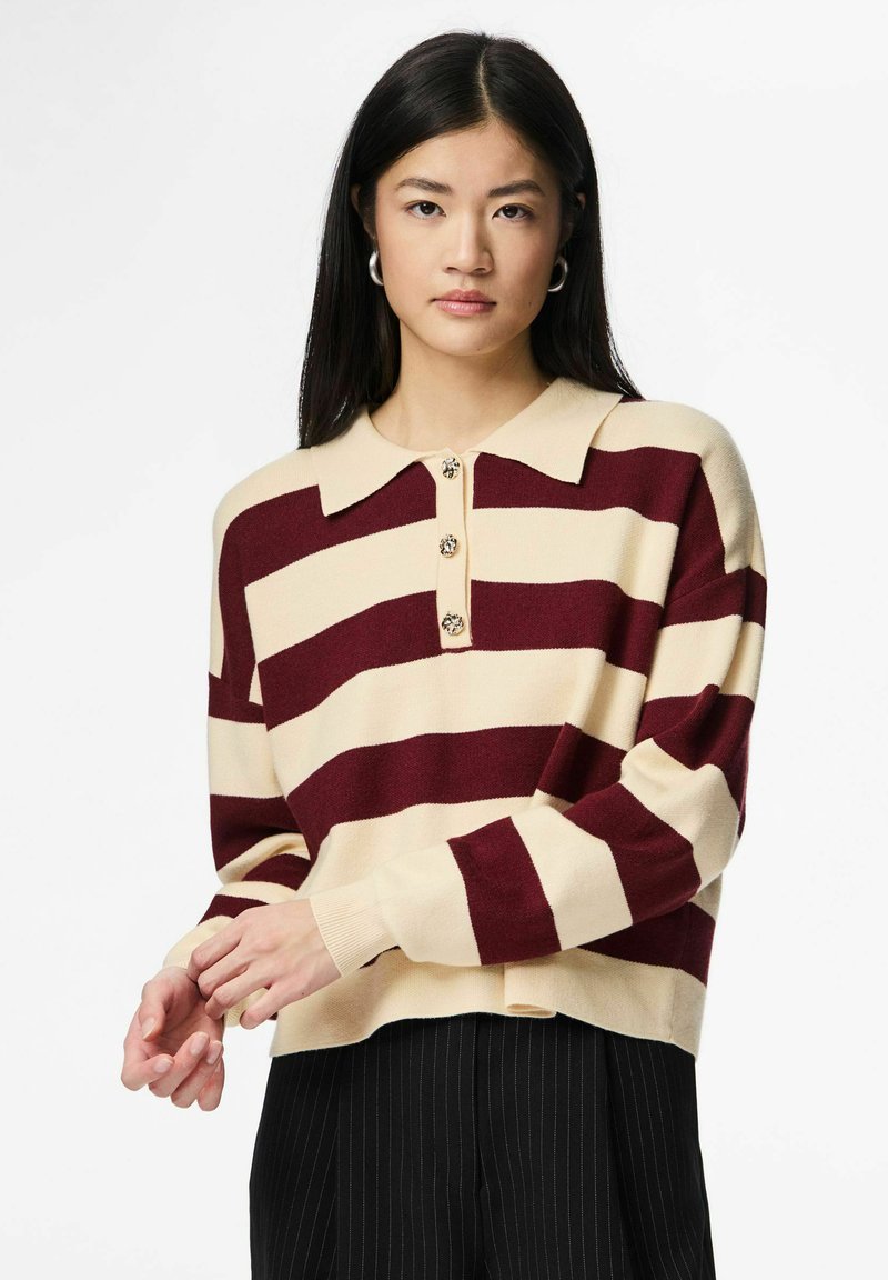 Adīts džemperis ar burgundijas un krēmkrāsas horizontālām svītrām, ar apkaklīti un četriem dekoratīviem pogām. Mīksta tekstūra, brīvs piegriezums.