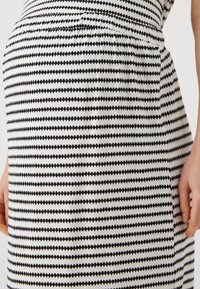 Šaty s černobílým pruhovaným vzorem, které mají shromážděný design vrchní části, zdůrazňují přiléhavý střih a jsou vyrobeny z jemného, lehkého materiálu.