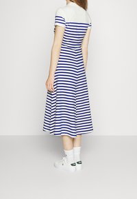 Niebieska i biała sukienka w paski z dopasowanym gorsetem i rozszerzanym dołem. Krótkie rękawy, kołnierzyk. Noszona z białymi trampkami i skarpetkami.