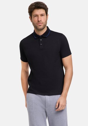 Schwarzes Poloshirt mit blauem Kragenakzent und drei Knöpfen, aus Baumwollmaterial, kombiniert mit hellgrauen Hosen.