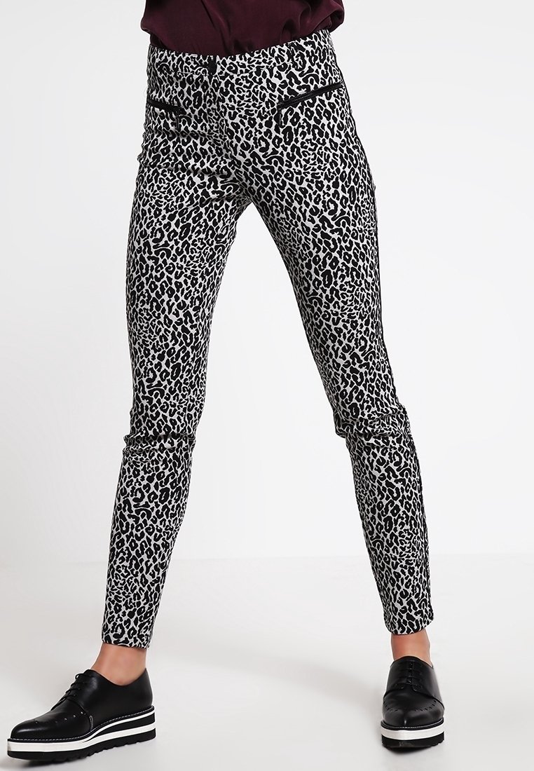 Pantalon slim à imprimé léopard noir et blanc, associé à des chaussures à plateforme noires à lacets et un haut sombre.