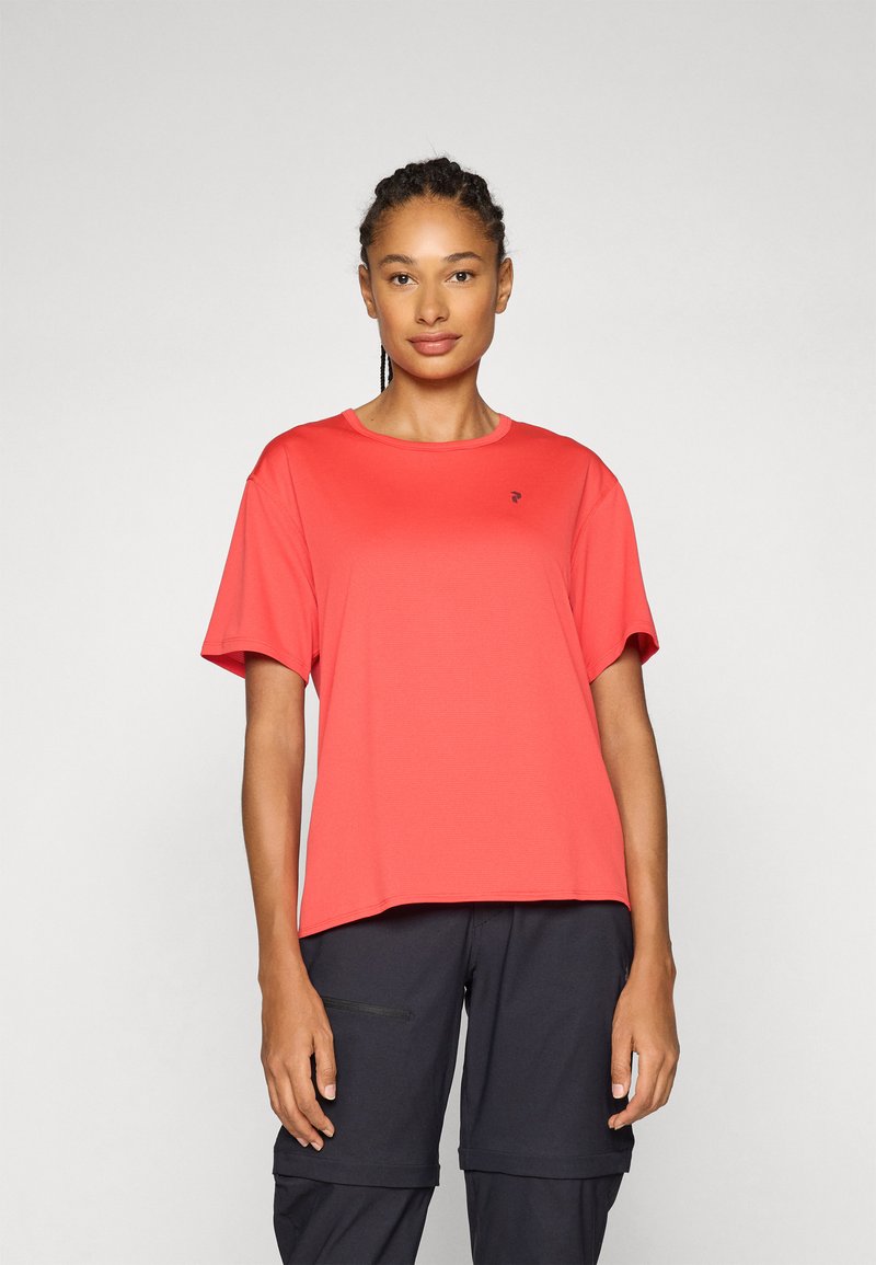 Coral short-sleeve t-shirt made of lightweight fabric, featuring a round neckline and a small logo on the chest. Paired with dark pants.