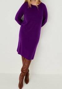 Vestito maglione viola a maniche lunghe con collo rotondo e superficie morbida, abbinato a stivali in pelle marrone al ginocchio.