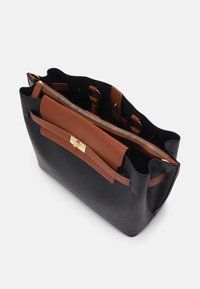 Sac cabas en cuir noir avec poche à rabat en cuir marron et compartiment supérieur à fermeture éclair, montré partiellement ouvert vu de dessus.