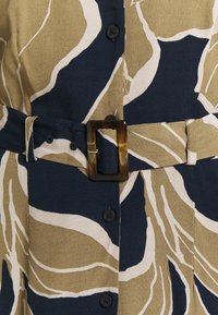 Koszula zapinana na guziki z botanicznym wzorem w kolorach granatowym, kremowym i oliwkowym. Posiada grubą, prostokątną sprzączkę w kolorze żółwia oraz regulowany pasek.