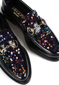 Czarne loafersy z cekinowym wierzchem, które mają wielokolorowe refleksy, złote akcenty metalowe oraz gładkie wykończenie z lakierowanej skóry.