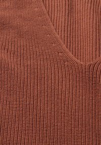 Gros plan sur un tissu tricoté côtelé couleur rouille avec détail d'encolure en V.