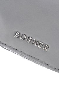 Portefeuille en tissu gris avec une surface texturée, arborant un logo "BOGNER" en relief argenté et un design épuré et minimal. Couture visible le long du bord.