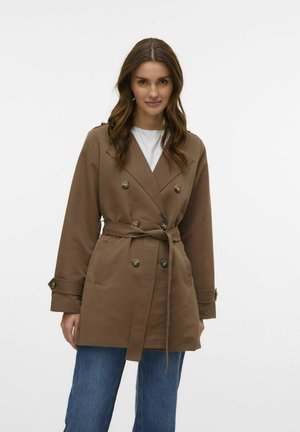 Manteau trench marron à double boutonnage avec une ceinture, présentant de grands boutons et une coupe ajustée, stylisé sur une chemise blanche et un jean bleu.