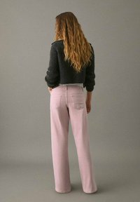 Suéter negro corto de punto con textura acanalada, acompañado de jeans de pierna ancha en rosa claro que cuentan con dos bolsillos traseros y un ajuste relajado.