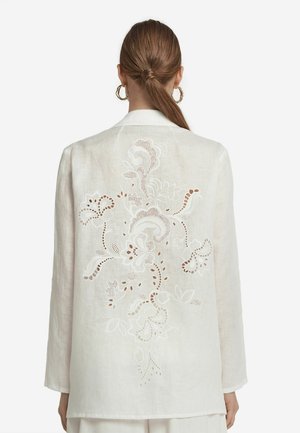 White linen blazer with long sleeves, featuring intricate floral embroidery and cut-out details on the back. Smooth texture.