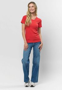 Raudona raištinė trumpomis rankovėmis marškinėlė su apvaliu iškirpimu, derinama su plačiomis mėlynomis džinsinėmis kelnėmis. Aprangoje yra pilki sportbačiai.