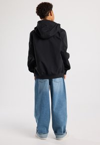 Schwarze Kapuzenjacke mit gerippten Bündchen, kombiniert mit weit geschnittenen, hellblauen Denim-Jeans. Der Stoff wirkt glatt und hat eine lockere Passform.