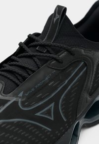 Zapatilla deportiva negra con una parte superior de malla transpirable, superposiciones sintéticas texturizadas y un sistema de amortiguación en ondas. Detalles en un azul más claro.